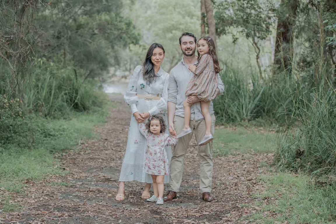 Family of four posing on a forest path, mother expecting a new baby.