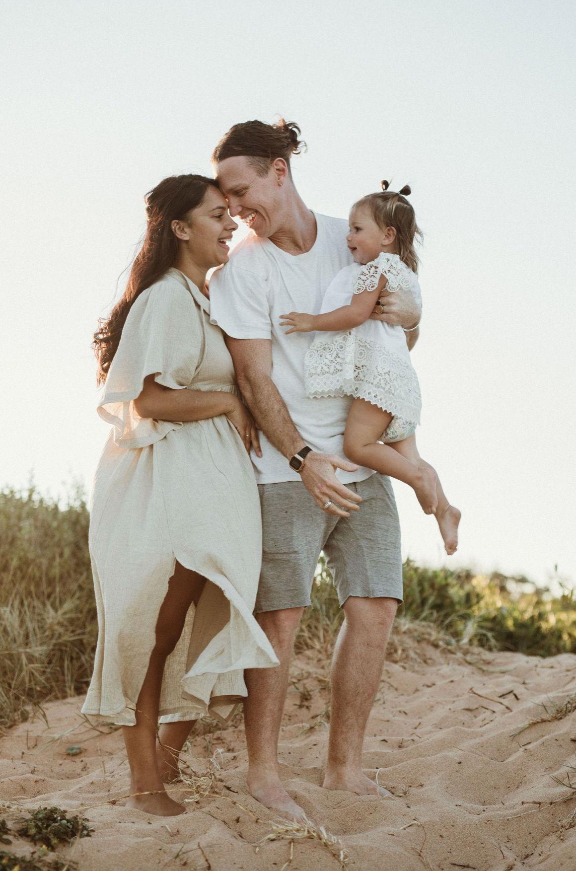 A happy family with a laughing toddler enjoys a sunny day on sandy dunes.