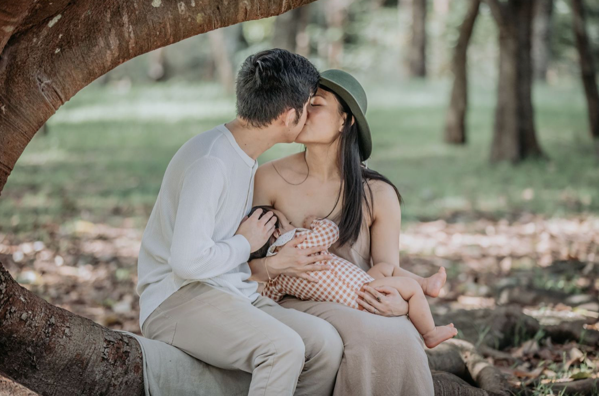 Couple sharing a kiss under a tree in a park during a maternity shoot.
