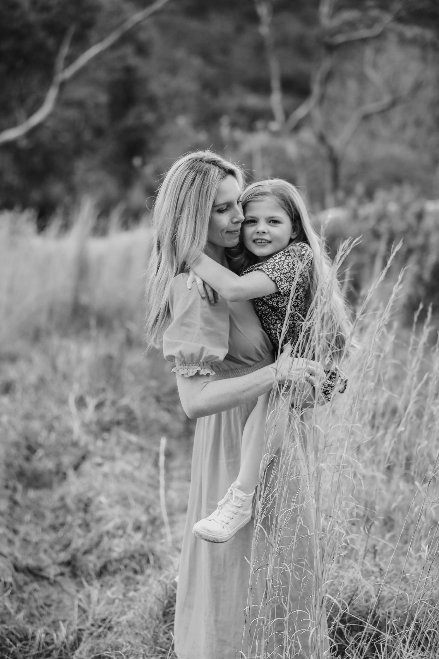 A blonde mother hugs her smiling young daughter in a field, black and white photo.