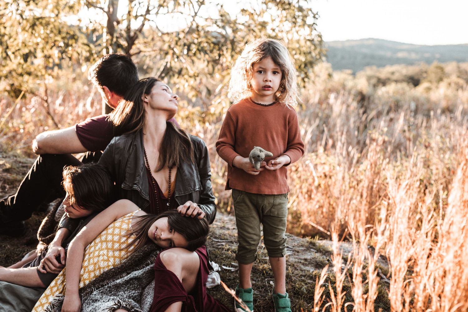 Mother and two children in golden field at sunset, boy holding small object.