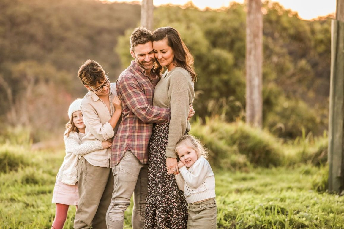 Loving family of five hugging and smiling together in a lush green field at golden sunset.