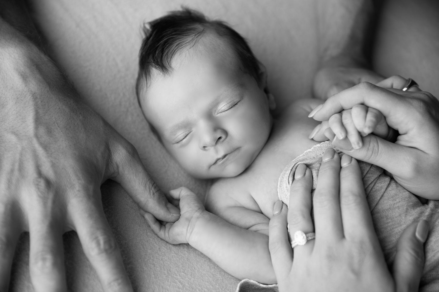 Black and white newborn baby sleeping peacefully while parents tenderly hold hands together in a touching family moment.