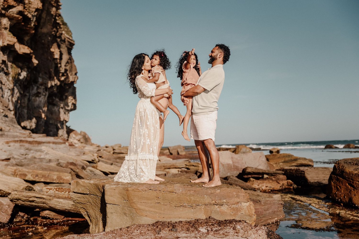 Family of four posing on coastal rocks during golden hour at the beach.
