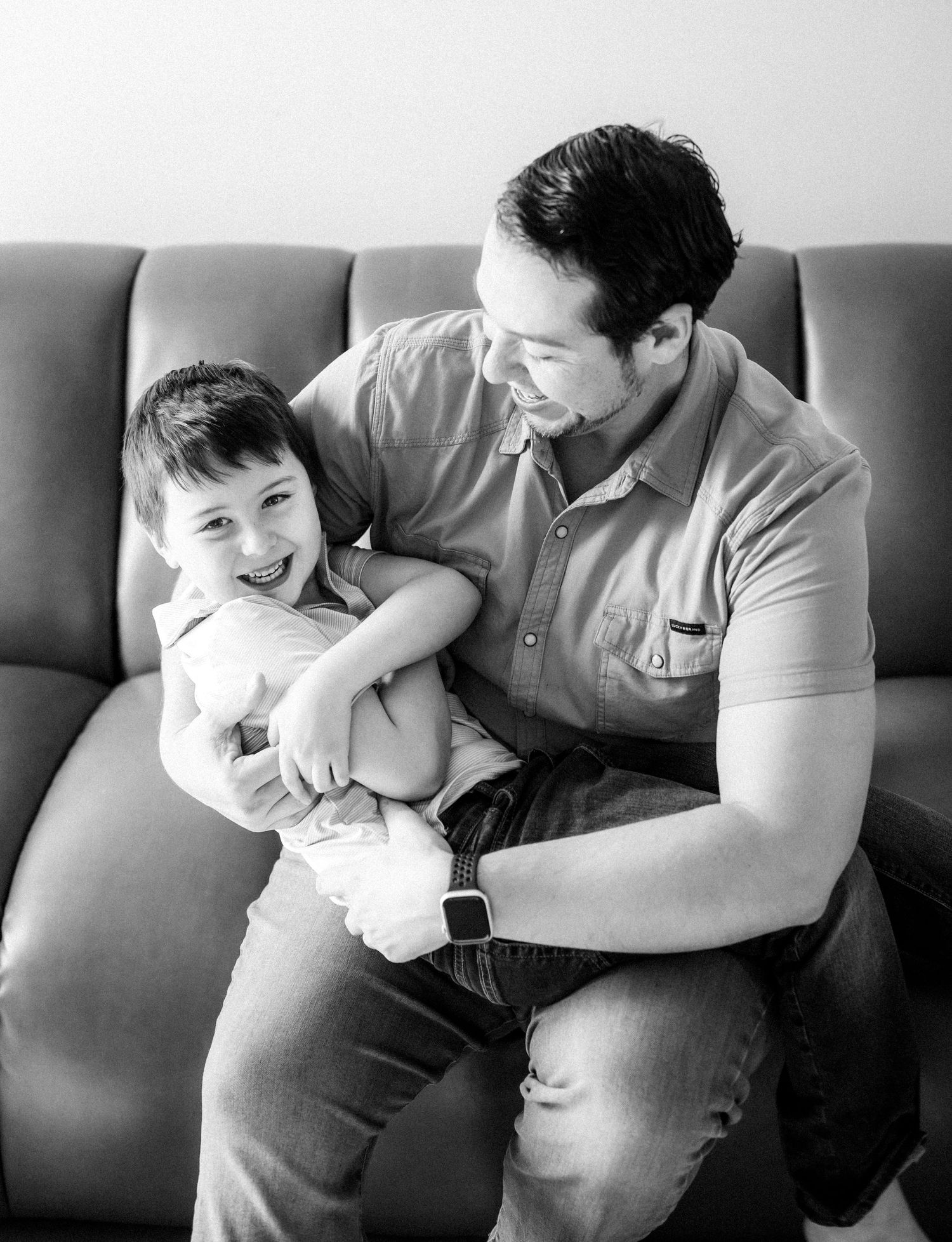 A black and white series of candid playful moments between a parent and child on a couch.