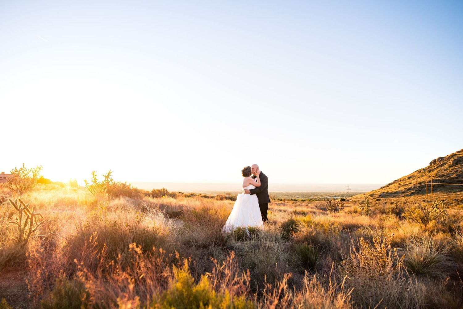 A couple embraces in silhouette against a golden sunset on a grassy hilltop during a romantic outdoor photoshoot.