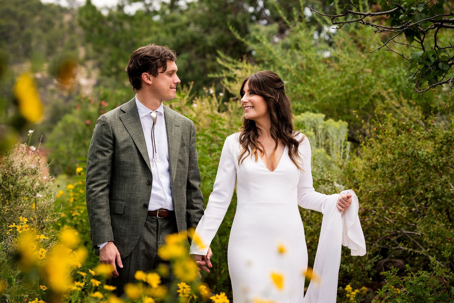 A couple embraces in a lush garden setting surrounded by yellow wildflowers on their wedding day at the Randal Davey Audubon in Santa Fe, NM