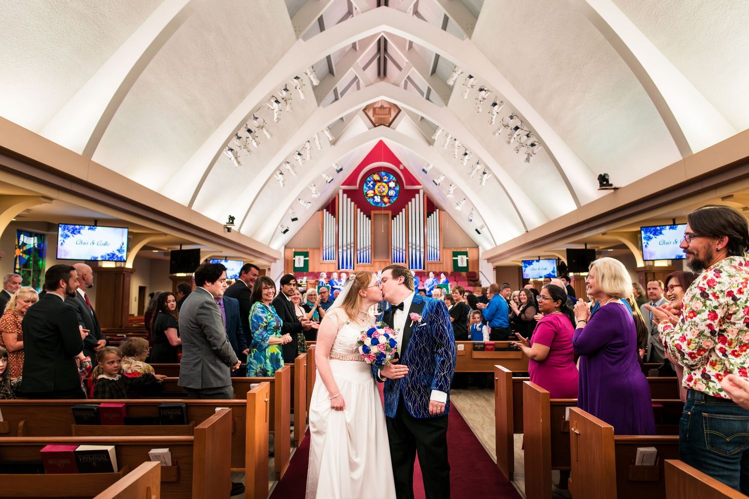 Wedding guests dance and celebrate on a crowded dance floor inside an elegant church reception venue with vaulted ceilings.