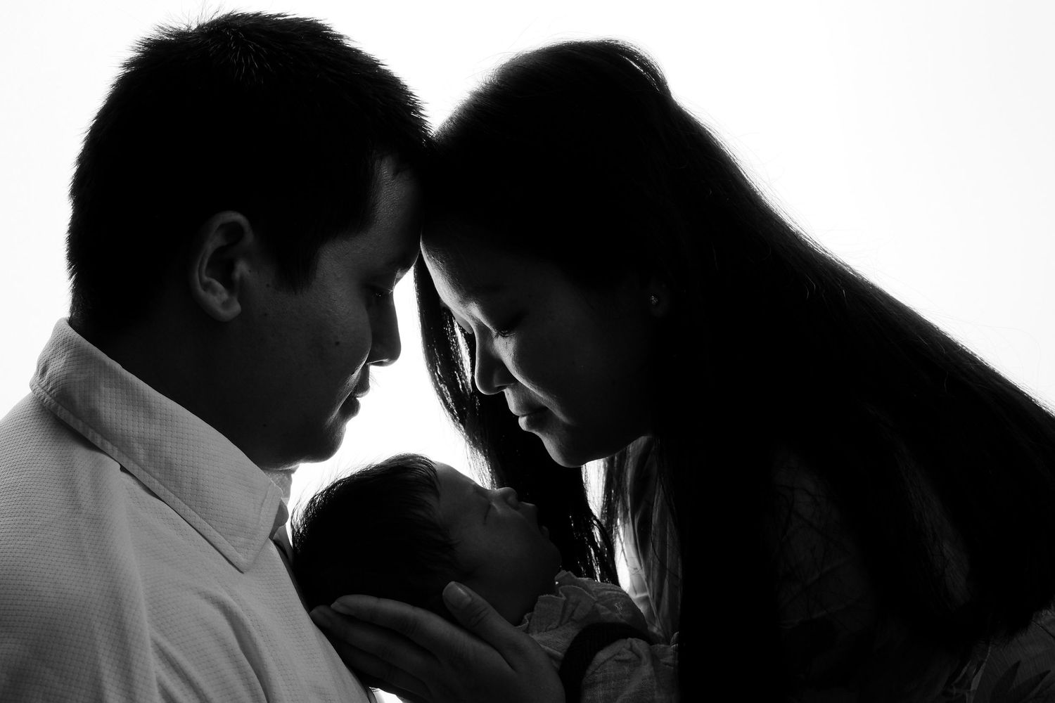 Intimate black and white silhouette of a family moment with a newborn baby.