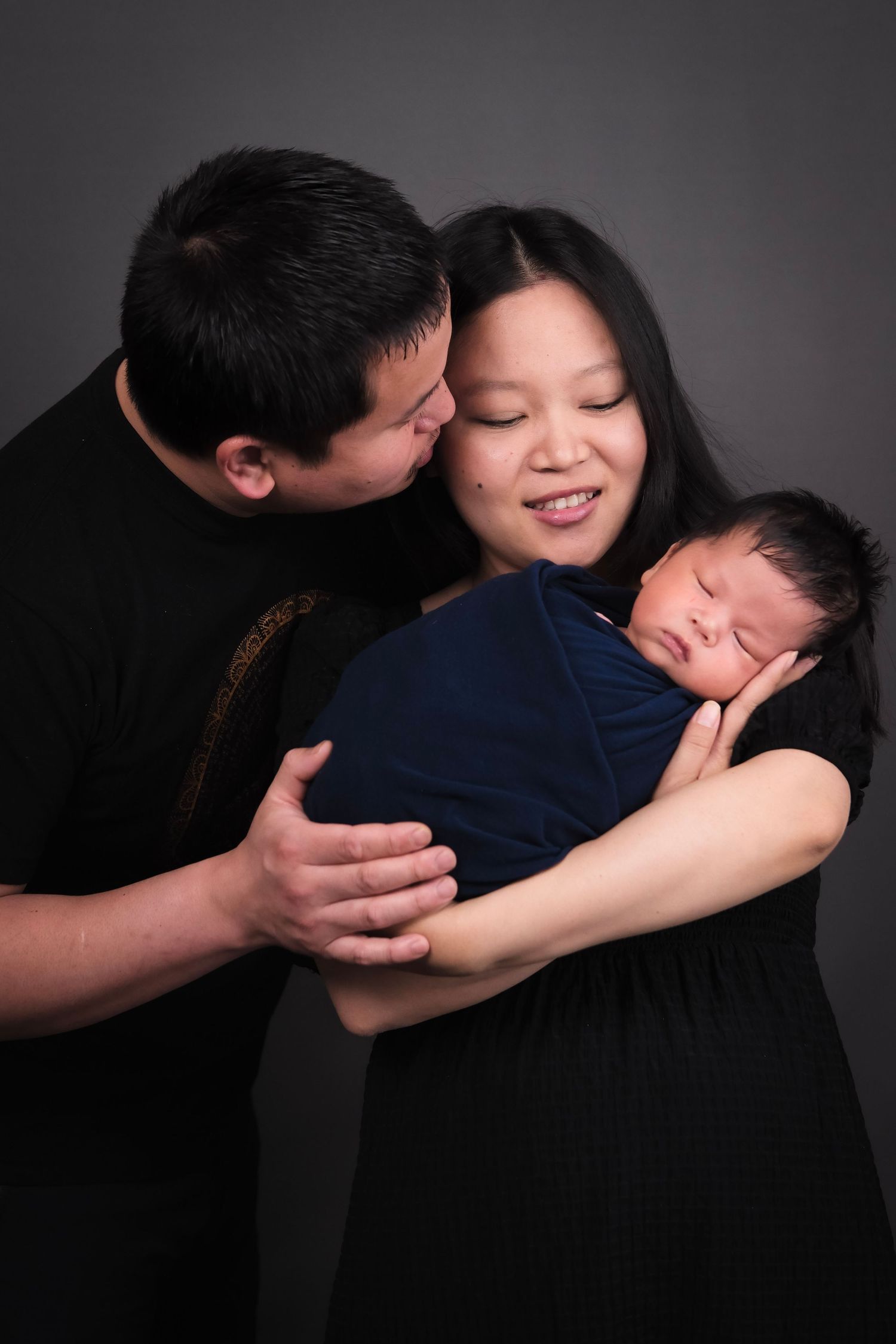 Family portrait series in dark tones showing tender moments with a newborn baby.