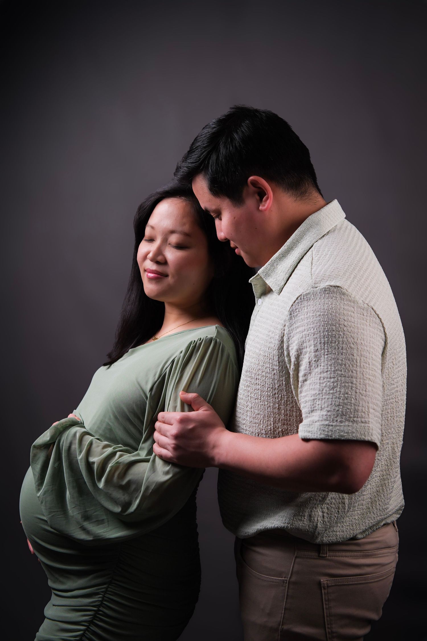 Artistic maternity portrait showing couple's intimate moment against dark backdrop.