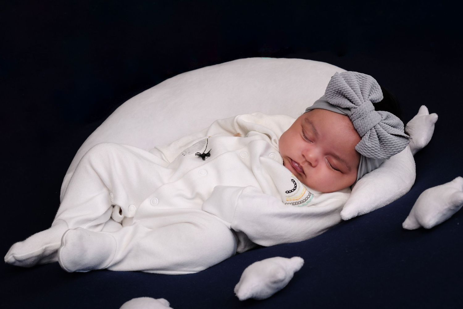 Newborn baby in white sleeper resting peacefully against black background with white stars.