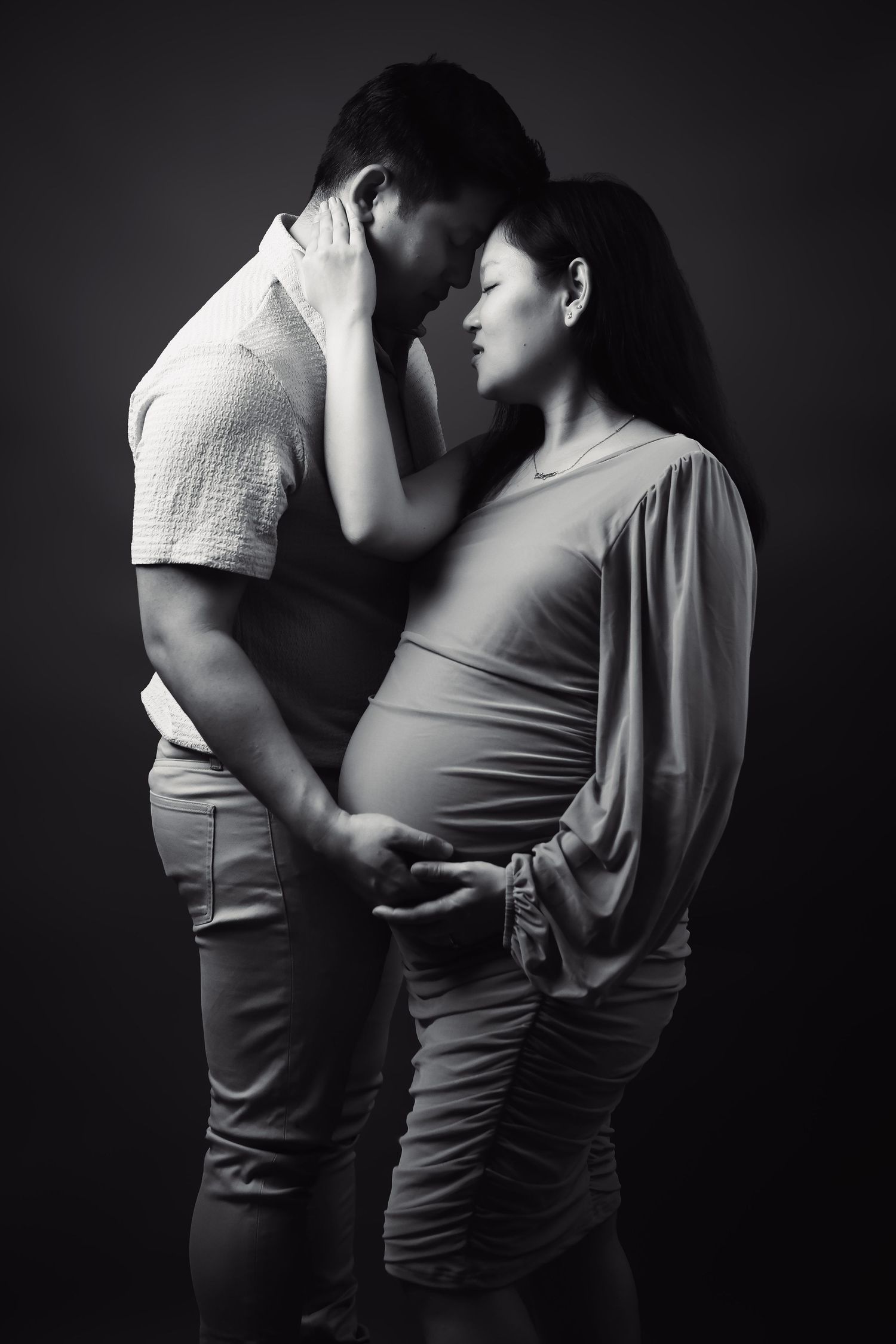 Intimate black and white maternity photo series showing couple embracing in dramatic lighting.