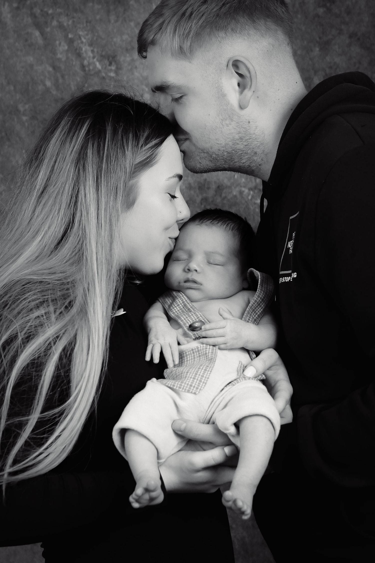Intimate black and white family portrait showing tender moment with newborn baby.