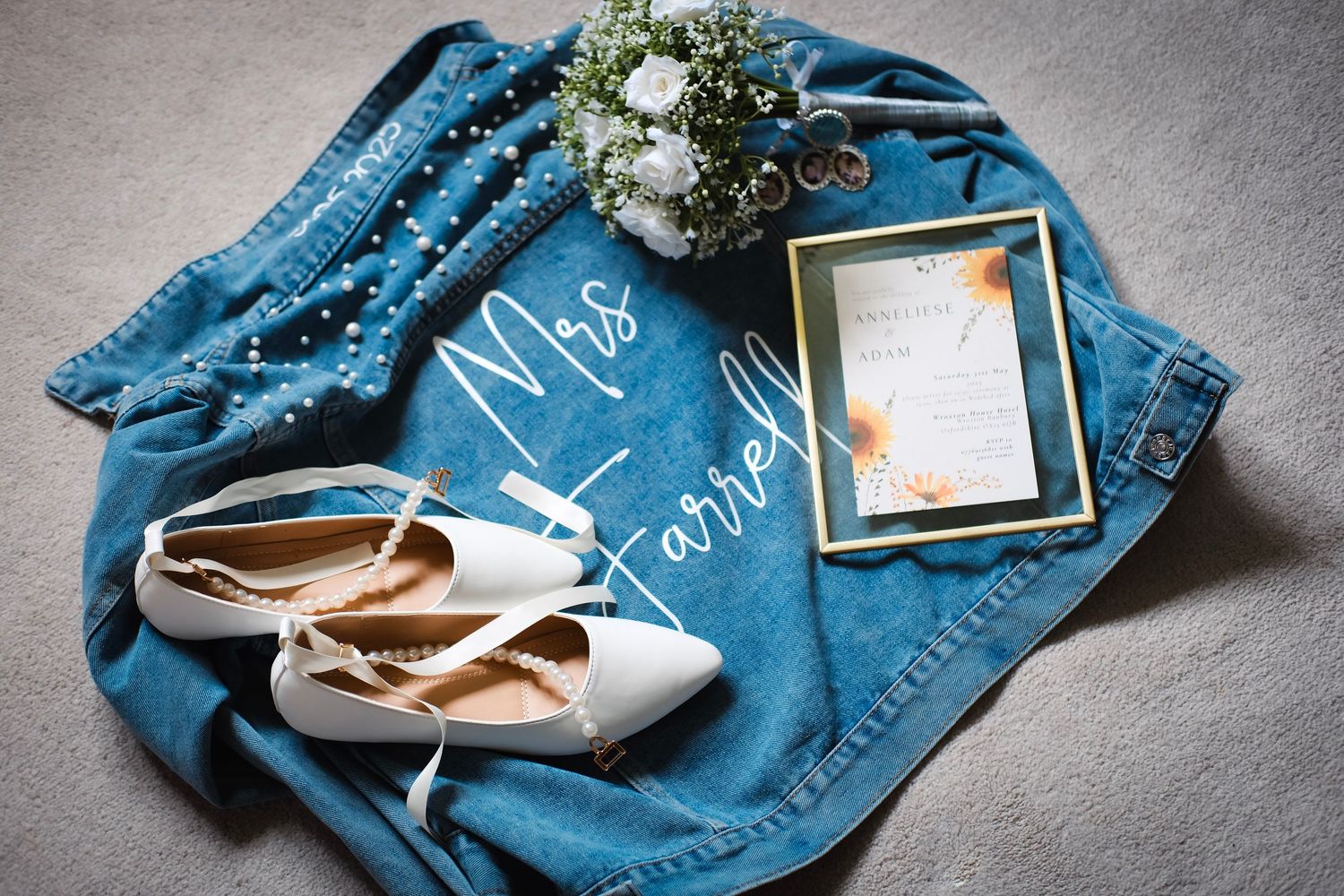 Wedding details featuring denim jacket, white shoes and invitation on gray background.