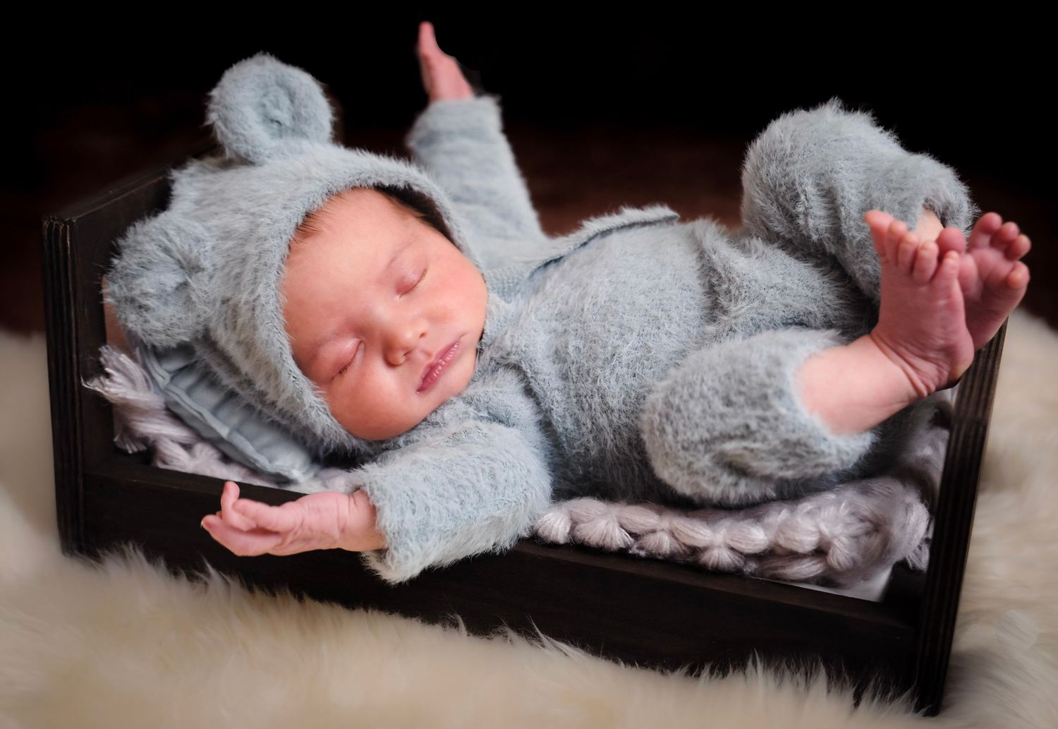 Newborn wearing gray knit outfit lying on textured backdrop.