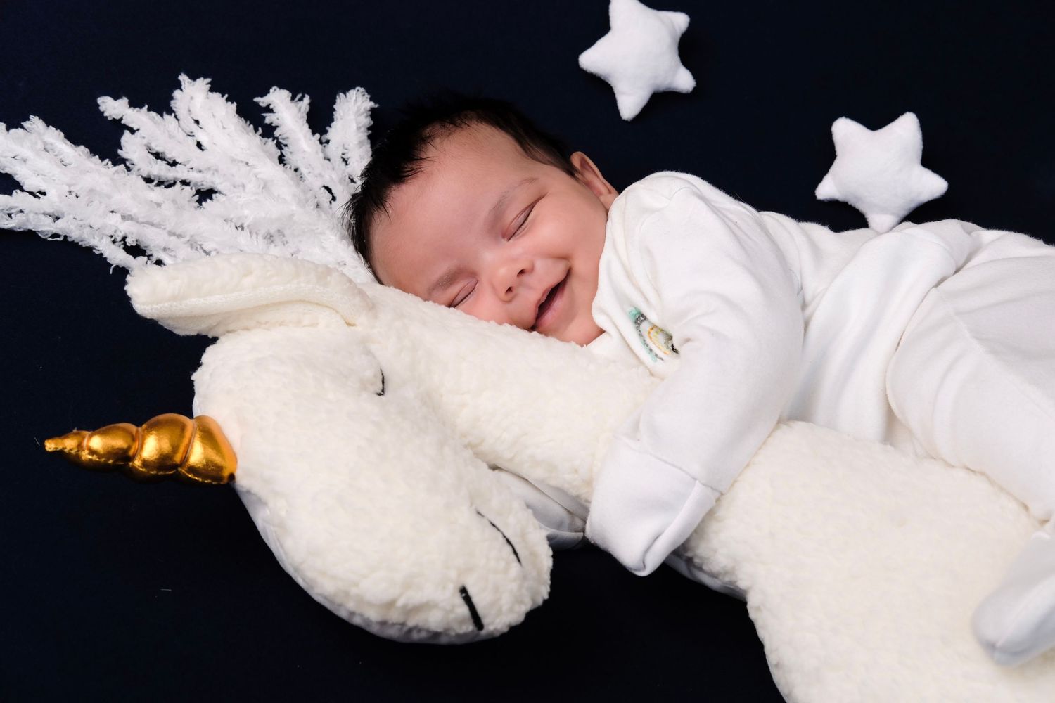 Baby resting on white crescent moon prop with decorative stars in studio setting.