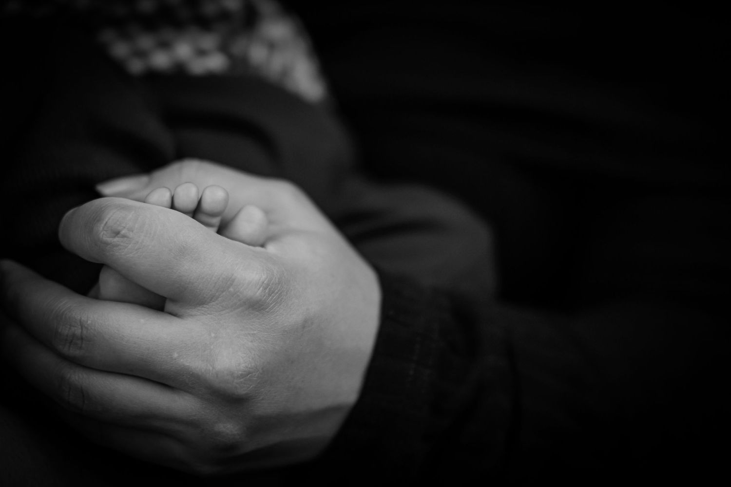 Close-up black and white photo of tiny newborn feet being gently held.