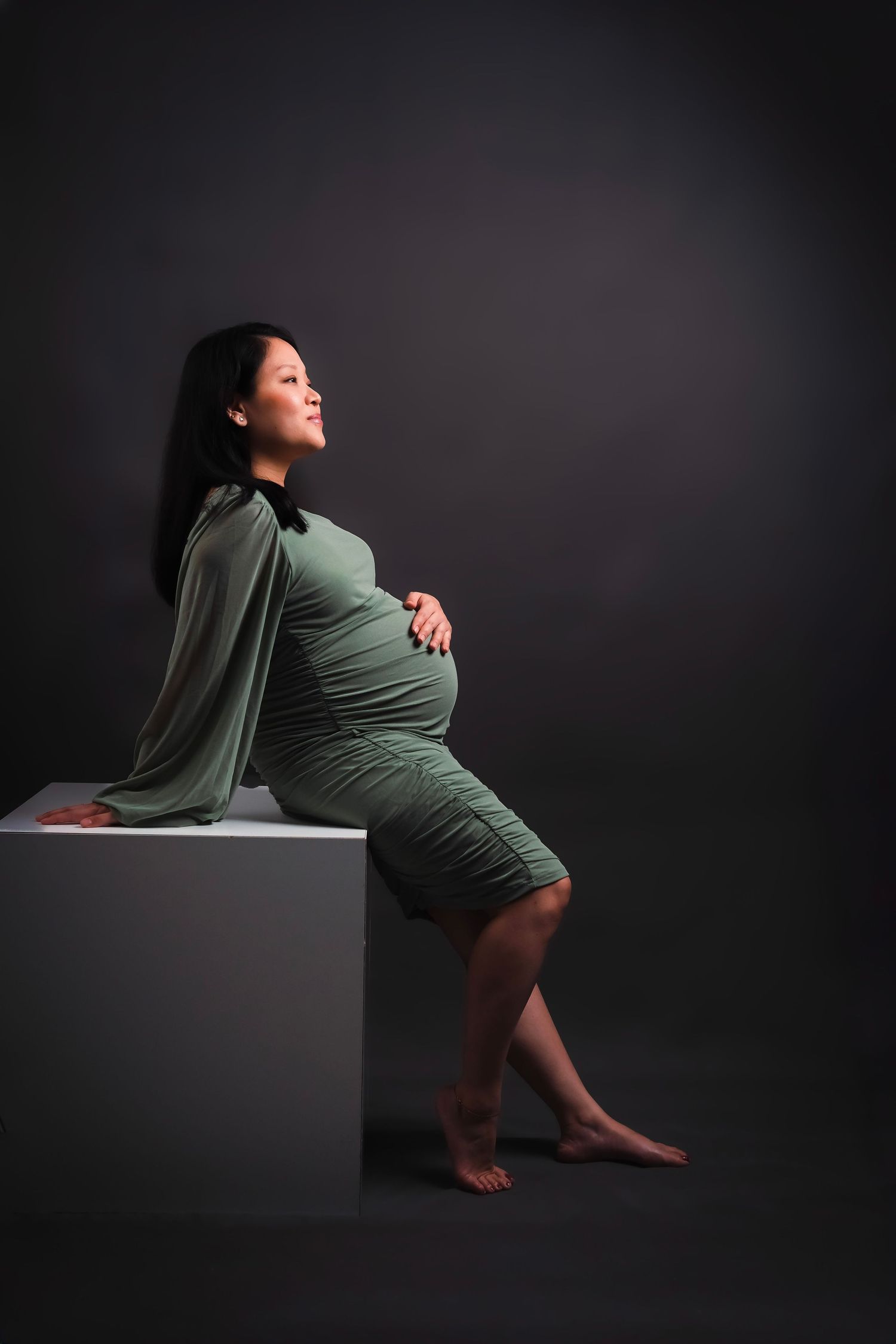 Studio maternity session with woman in green dress creating dramatic poses on black cube.