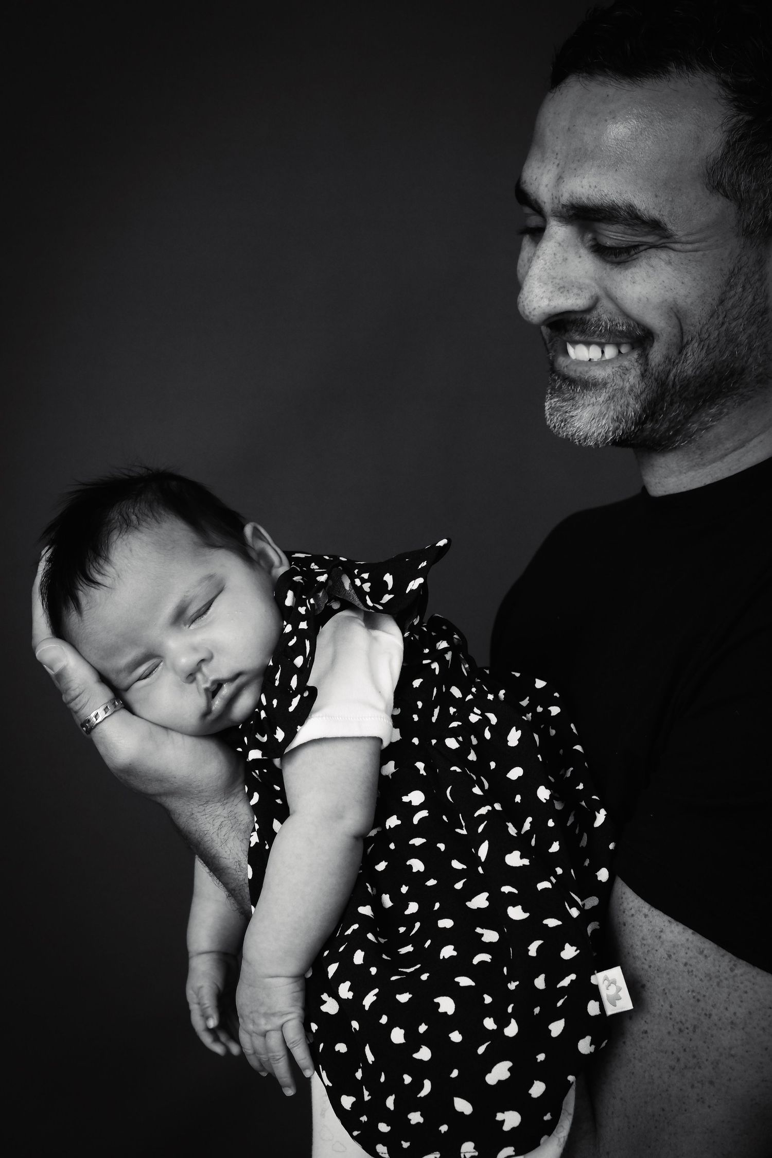Peaceful sleeping baby held gently in dramatic black and white portrait sequence.