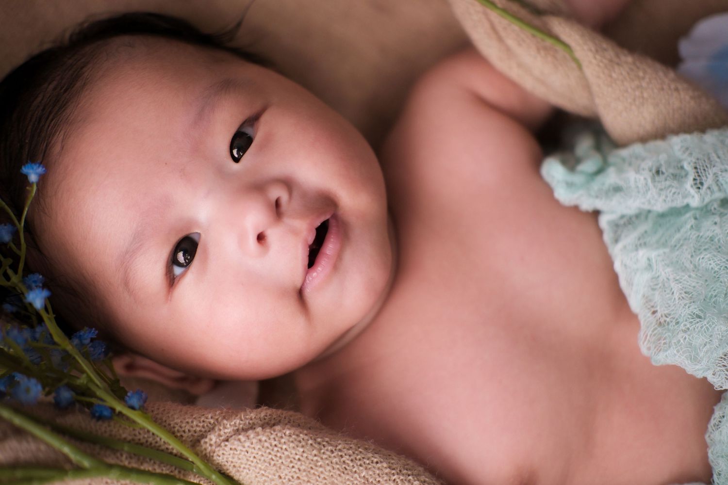 Sweet portrait of baby in delicate lace outfit laying on soft fabric.