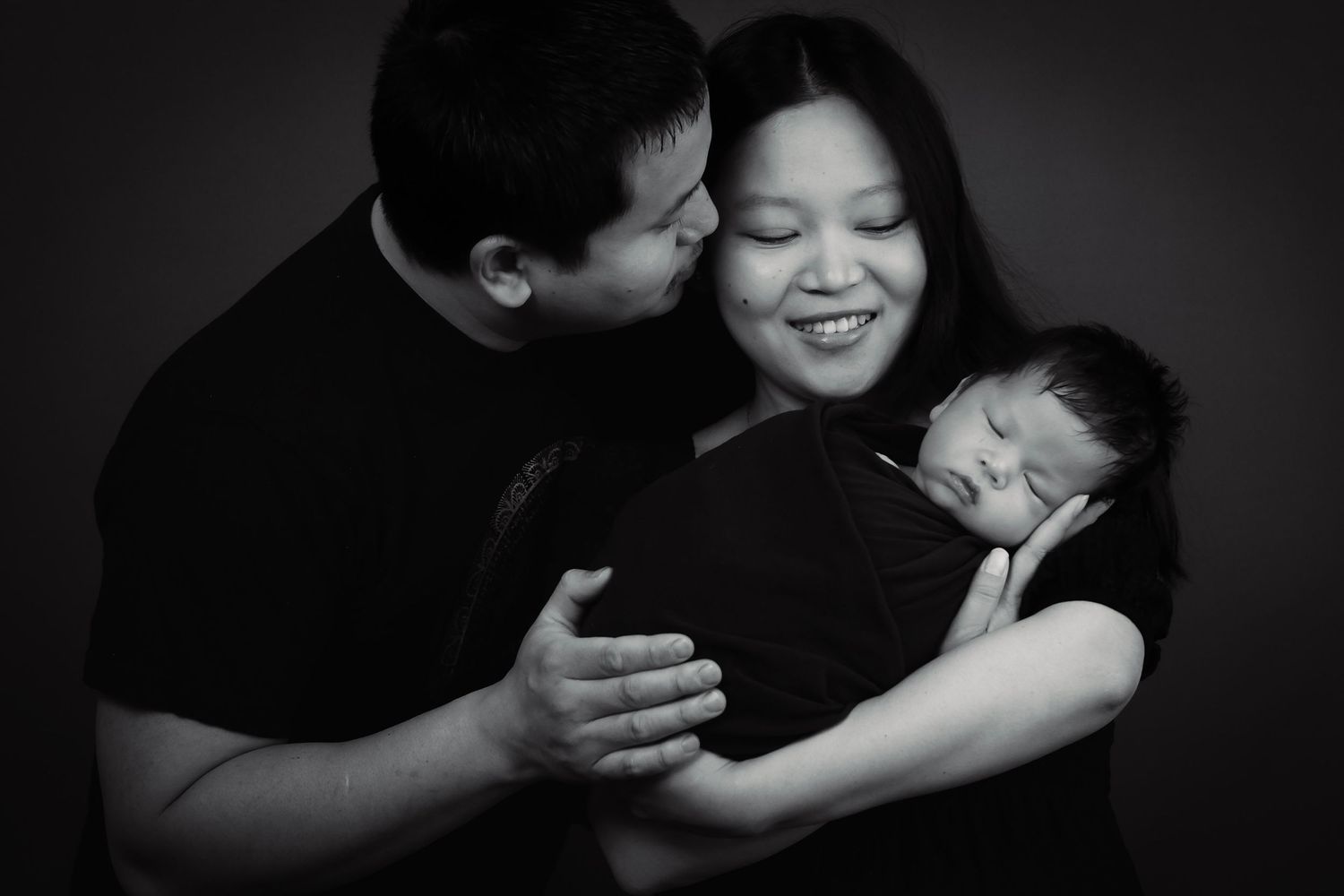 Black and white portrait of tender family moment with sleeping newborn.