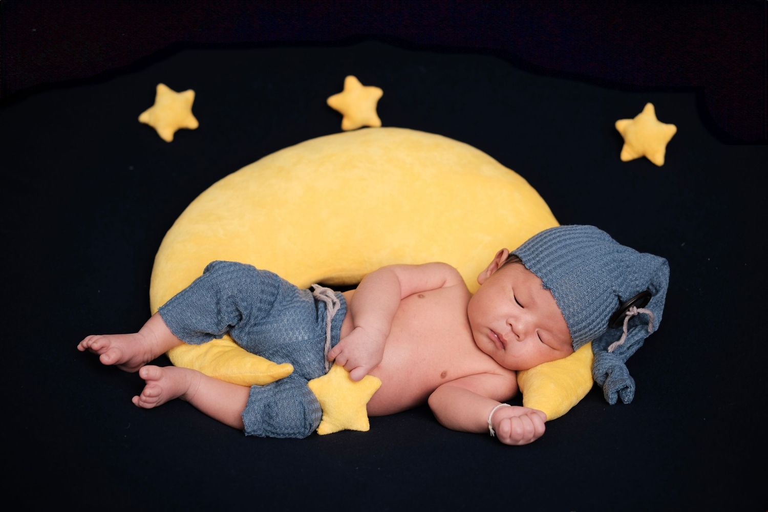 Sleeping newborn on yellow crescent moon prop with decorative stars.