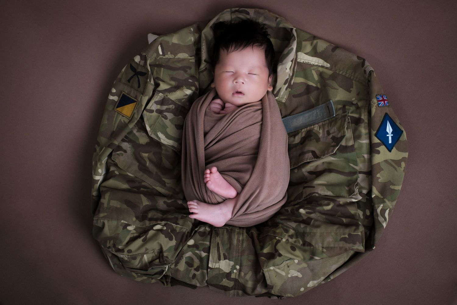 A series of six photos showing a sleeping baby wrapped in brown fabric resting on military camouflage material.