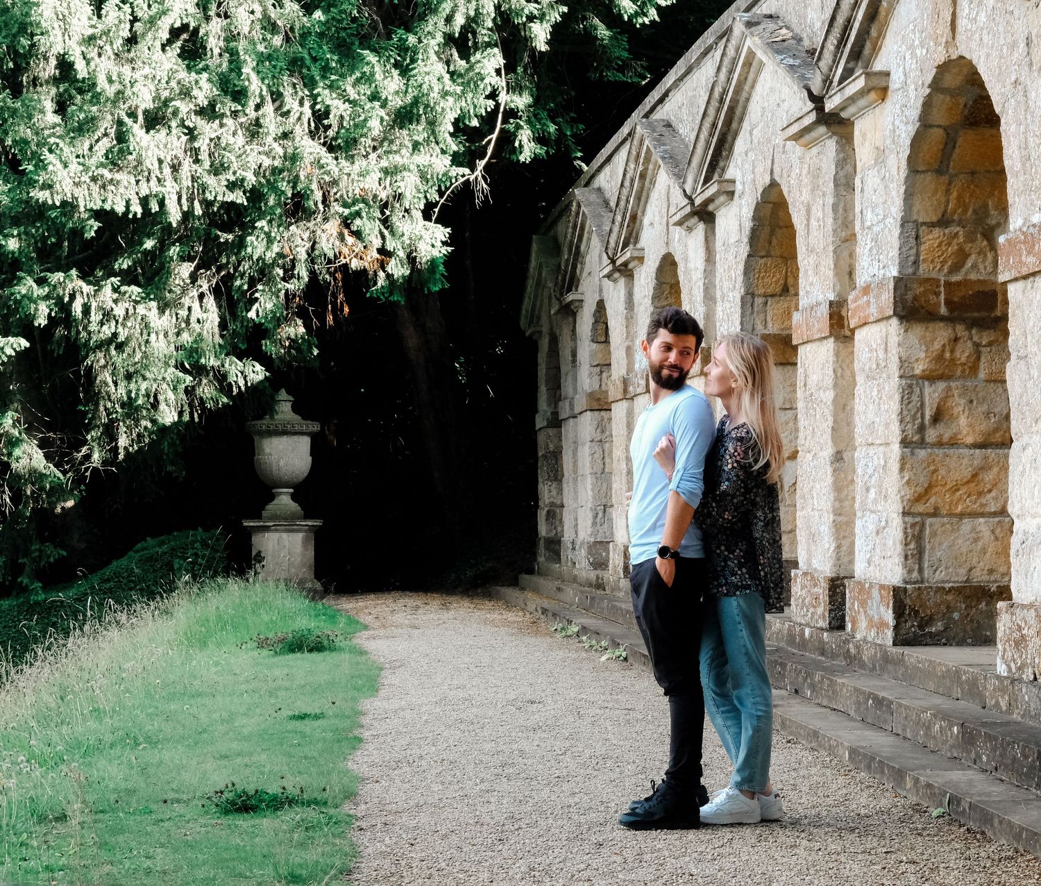 Stone archway walkway with lush greenery and decorative architectural details in an outdoor setting.