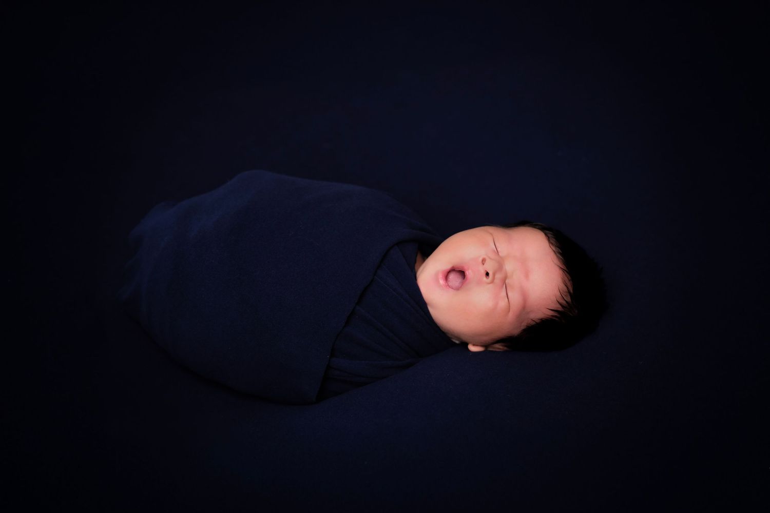 Artistic newborn portrait series with dark background and dramatic lighting.