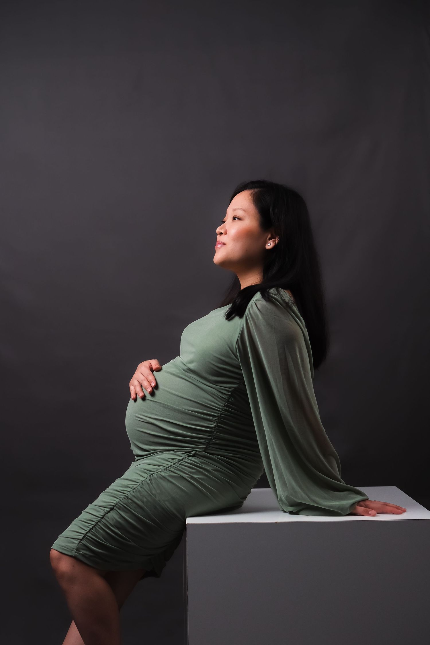 Dramatic studio maternity portraits showing woman in green dress against dark background.