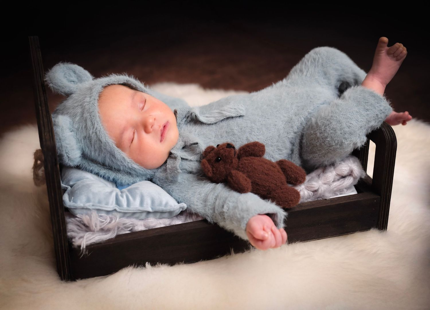 Sleeping newborn in gray outfit on textured surface with dramatic lighting.