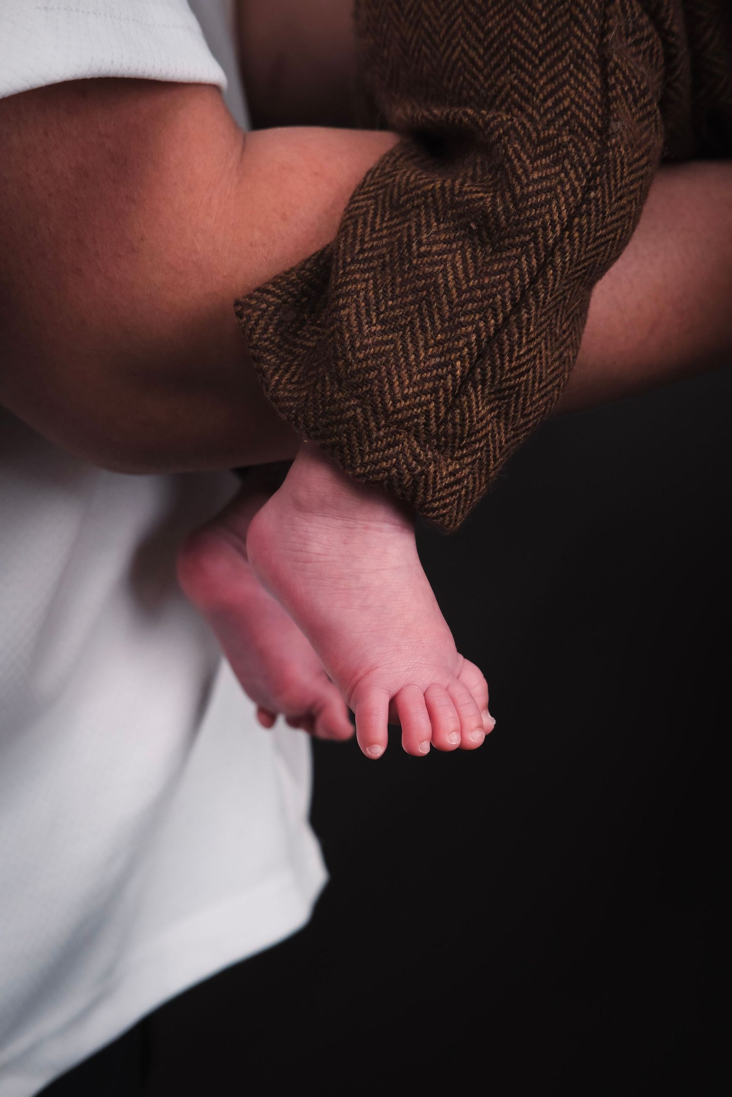 Close-up of tiny baby feet against herringbone fabric and white clothing.