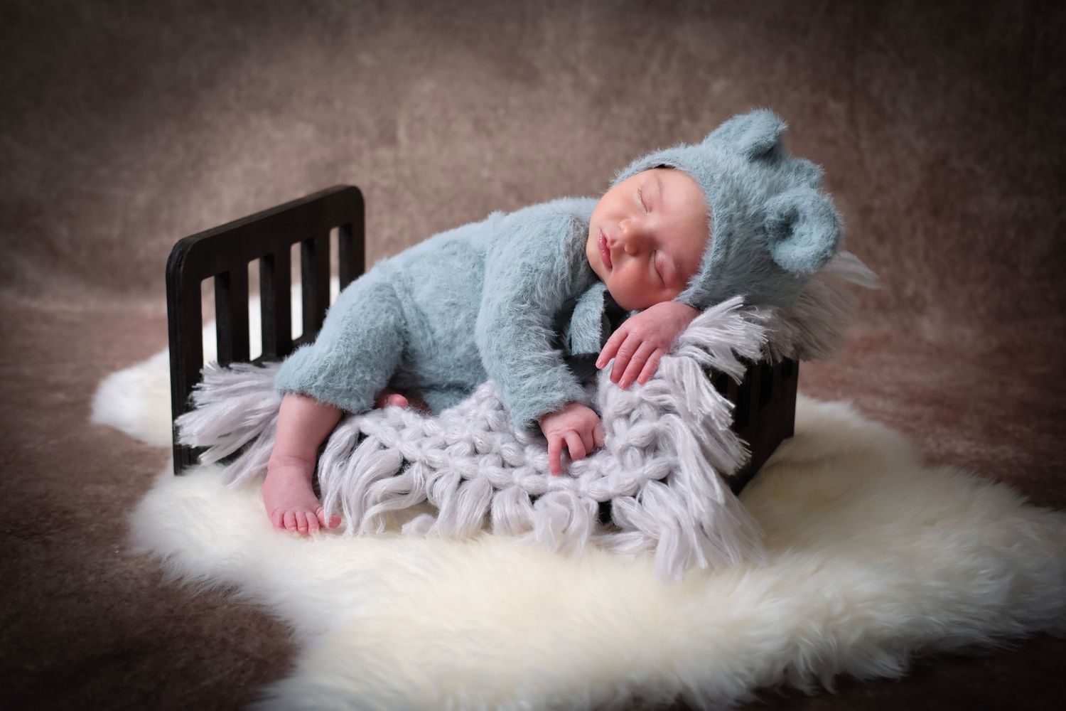 Newborn baby sleeping peacefully on soft white fur blanket in artistic black and white portrait series.