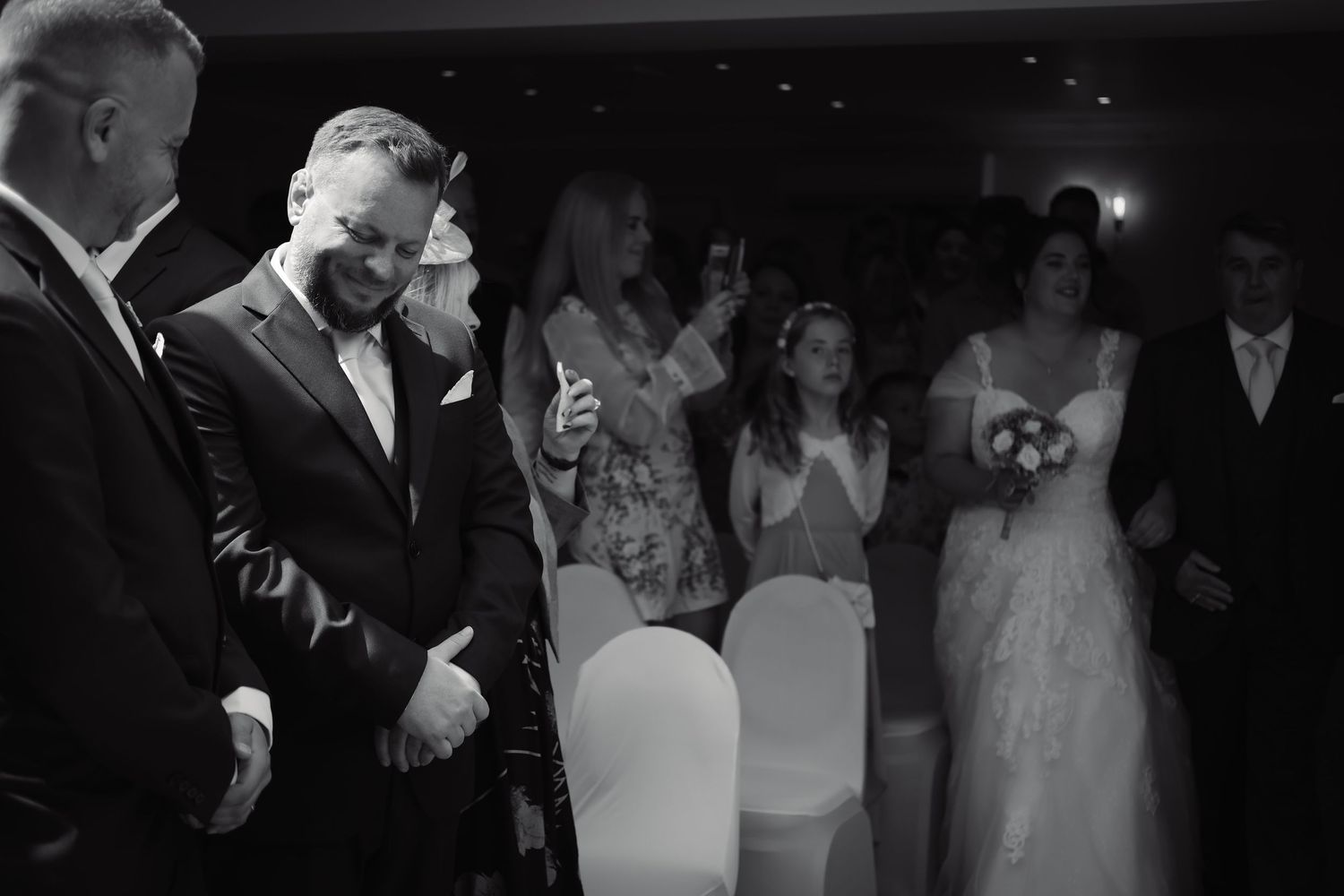 Black and white candid photo of wedding guests sharing joyful moment during ceremony.