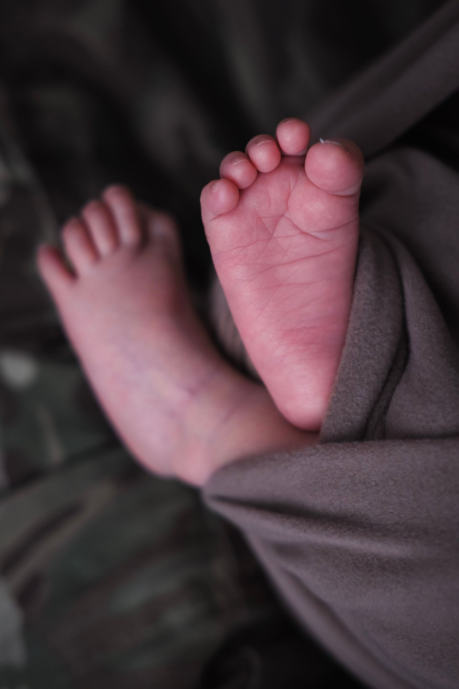 Close-up of tiny newborn baby feet wrapped in gray fabric against dark background.