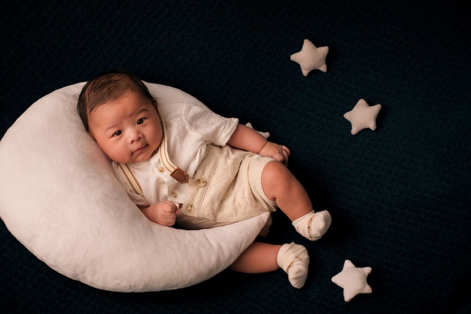 Peaceful newborn sleeping on crescent moon pillow surrounded by star decorations.