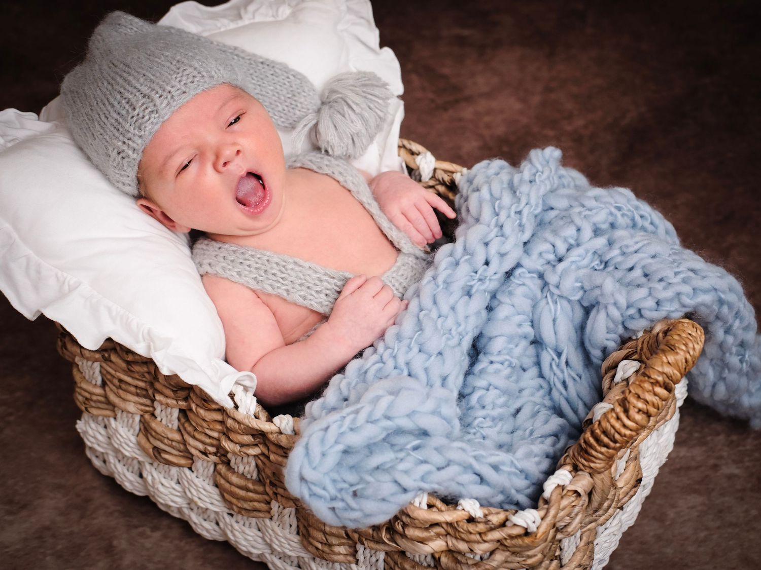 Sleeping newborn in wicker basket with blue blanket and delicate styling.