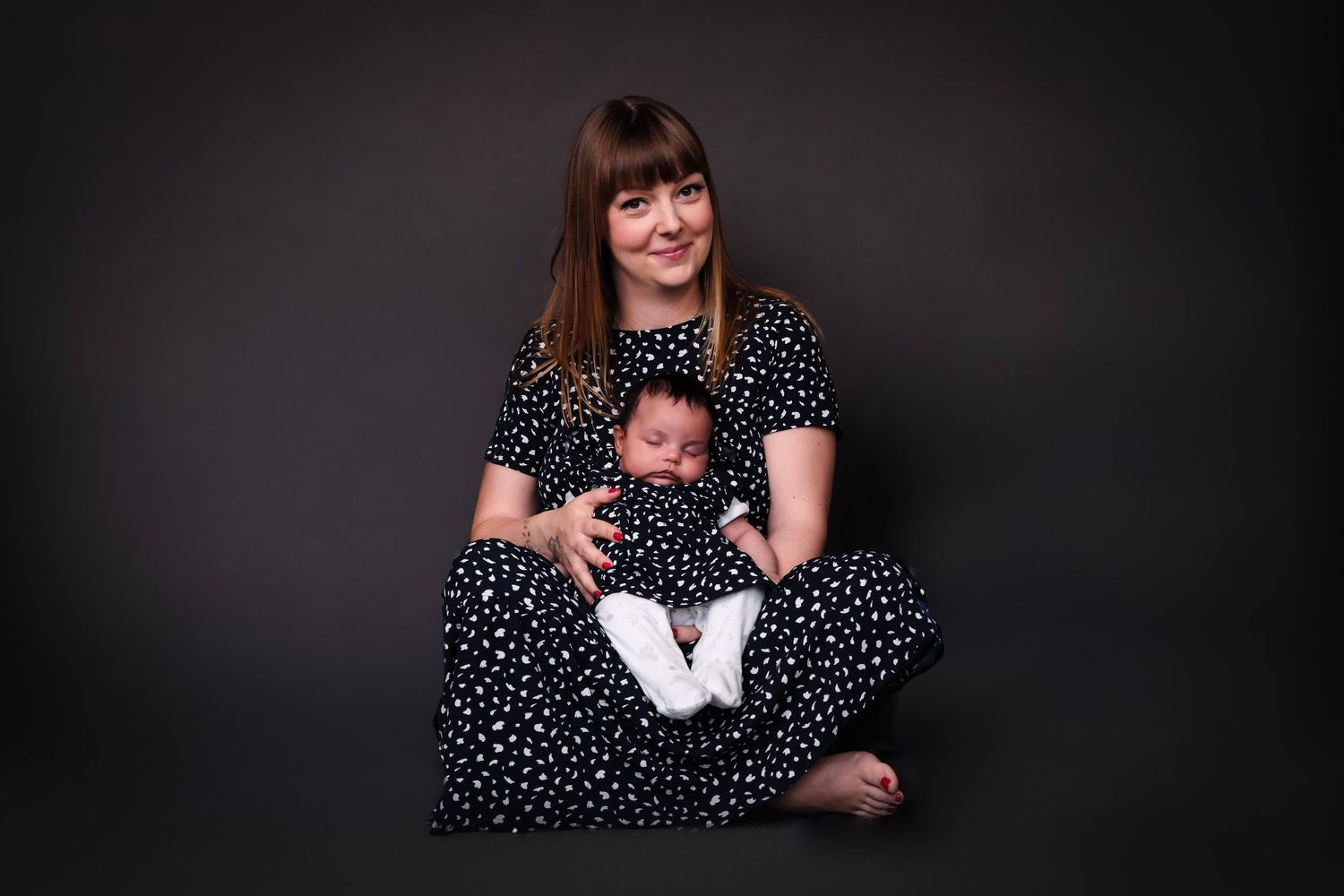 Mother and baby in matching polka dot outfits pose against dark background.