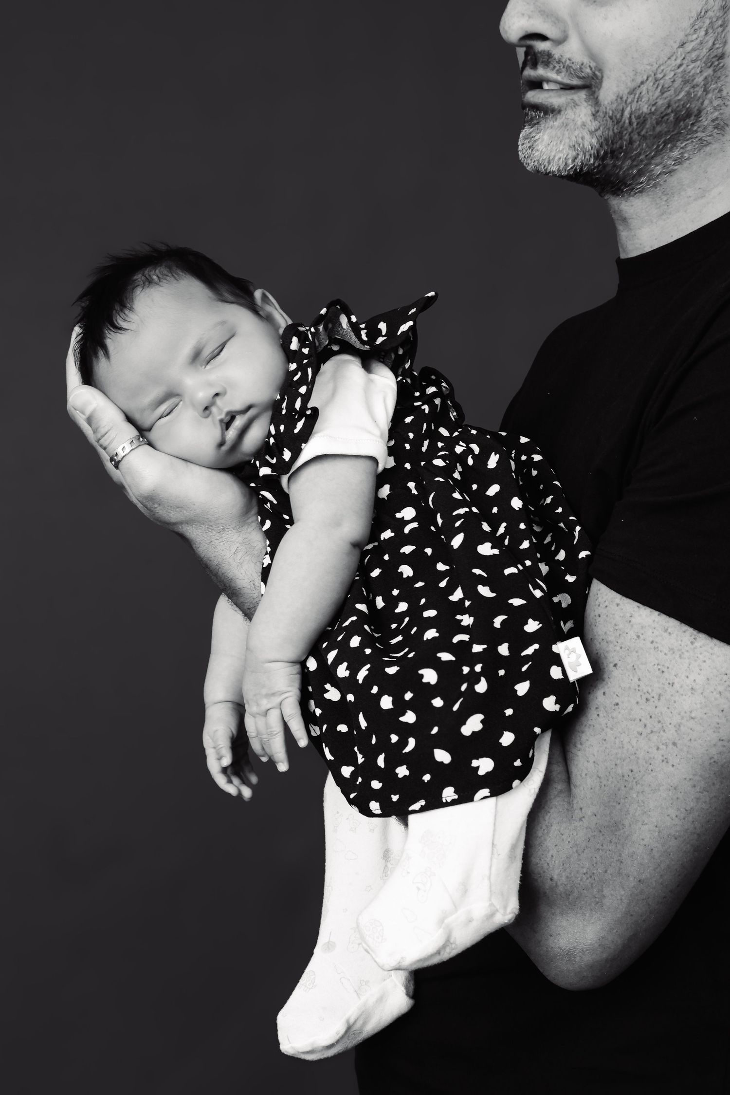 Black and white portrait of sleeping baby in polka dot dress being held.