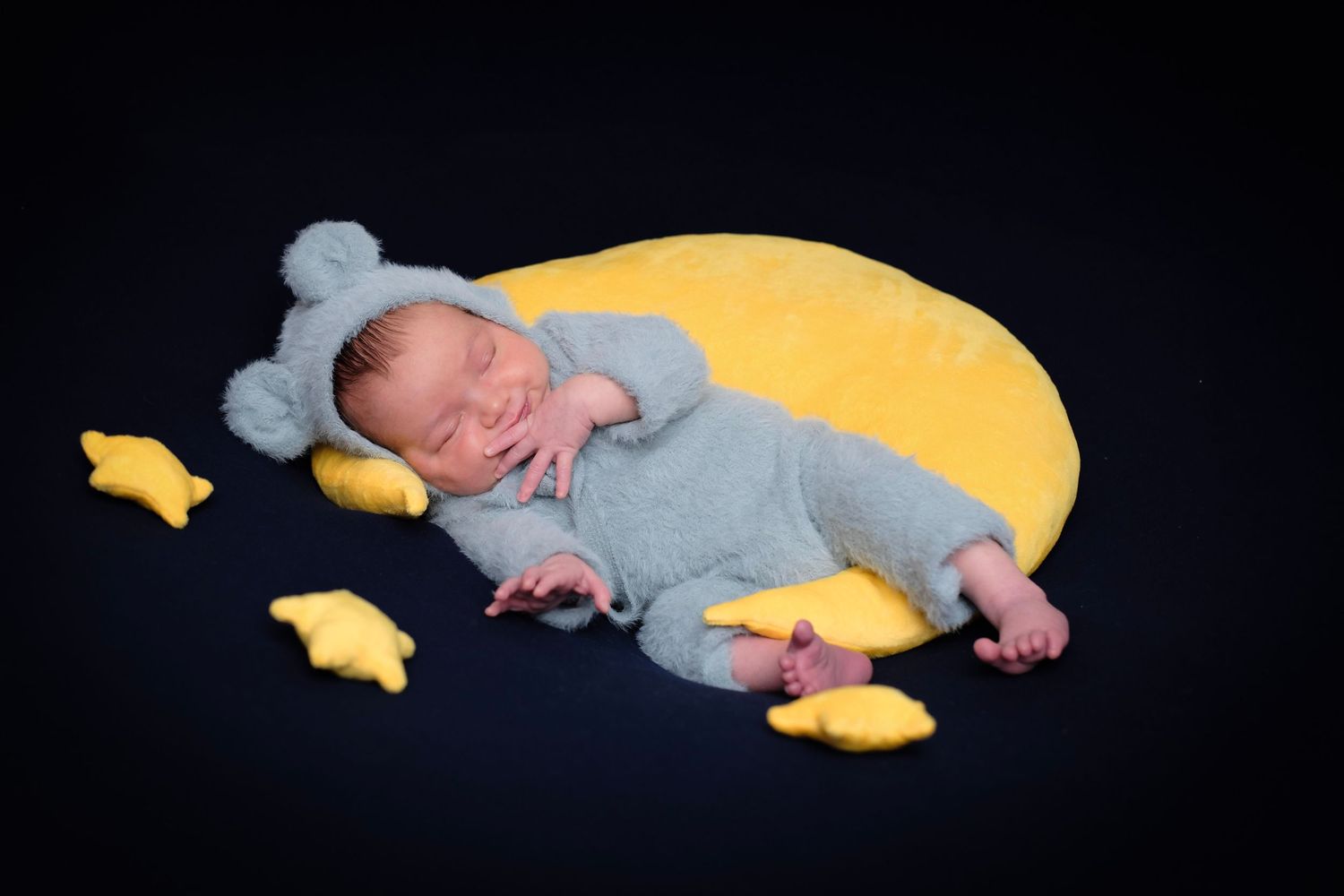 Sleeping baby in grey outfit resting on yellow moon-shaped pillow with star decorations.