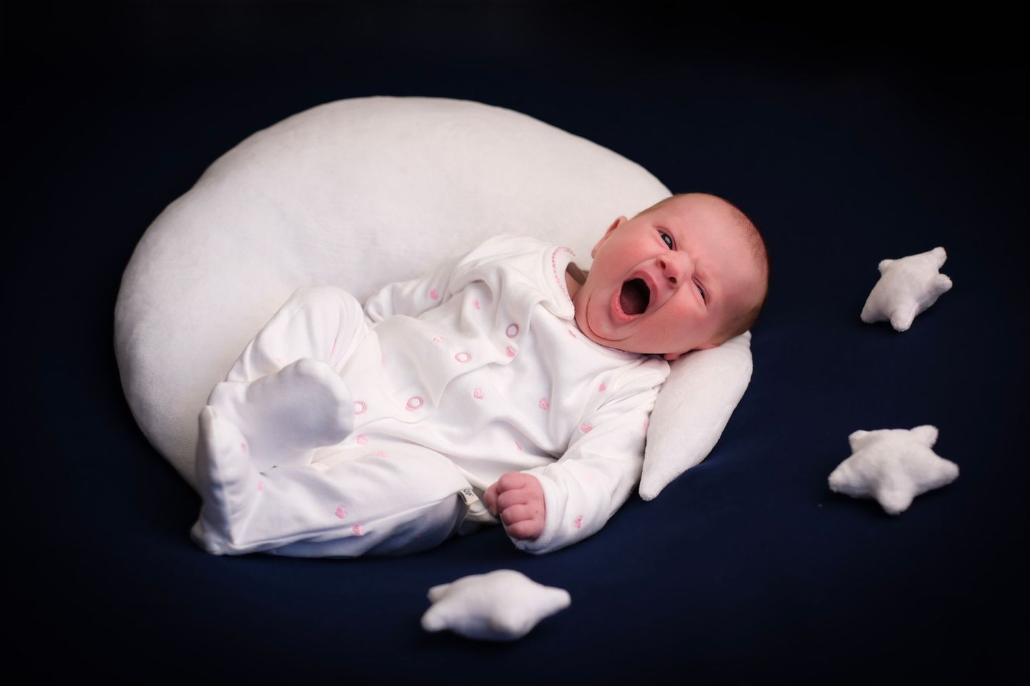 Sleeping newborn in white outfit with star decorations against dark background.