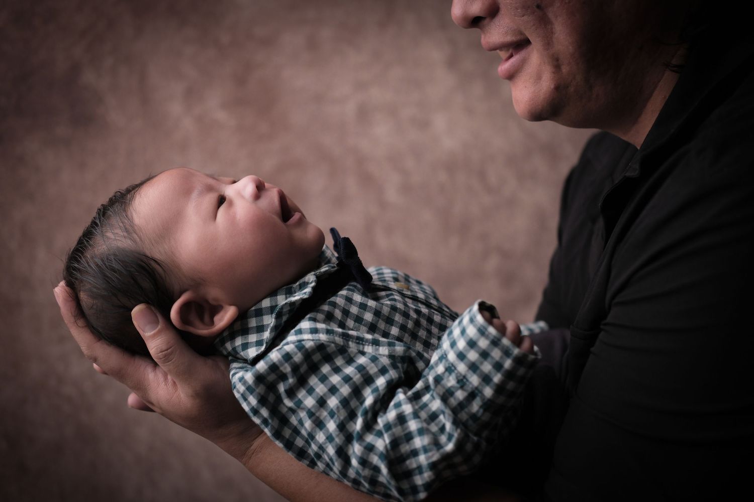 Baby in checkered outfit rests peacefully in gentle embrace.