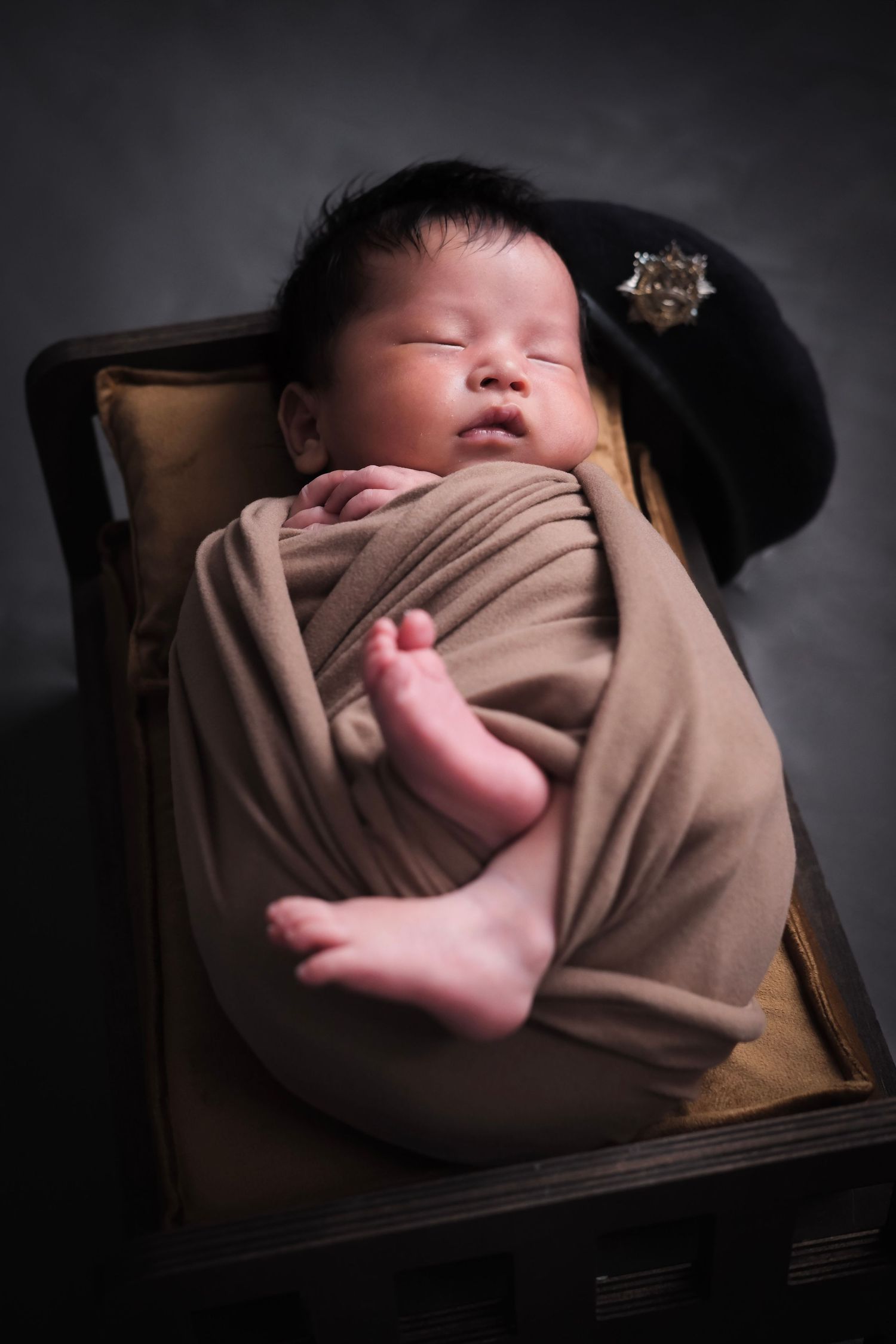 Sleeping newborn wrapped in brown fabric with tiny feet peeking out.