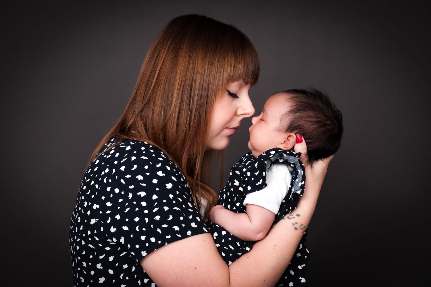 Emotional black and white family portrait with polka dot clothing against dark backdrop.