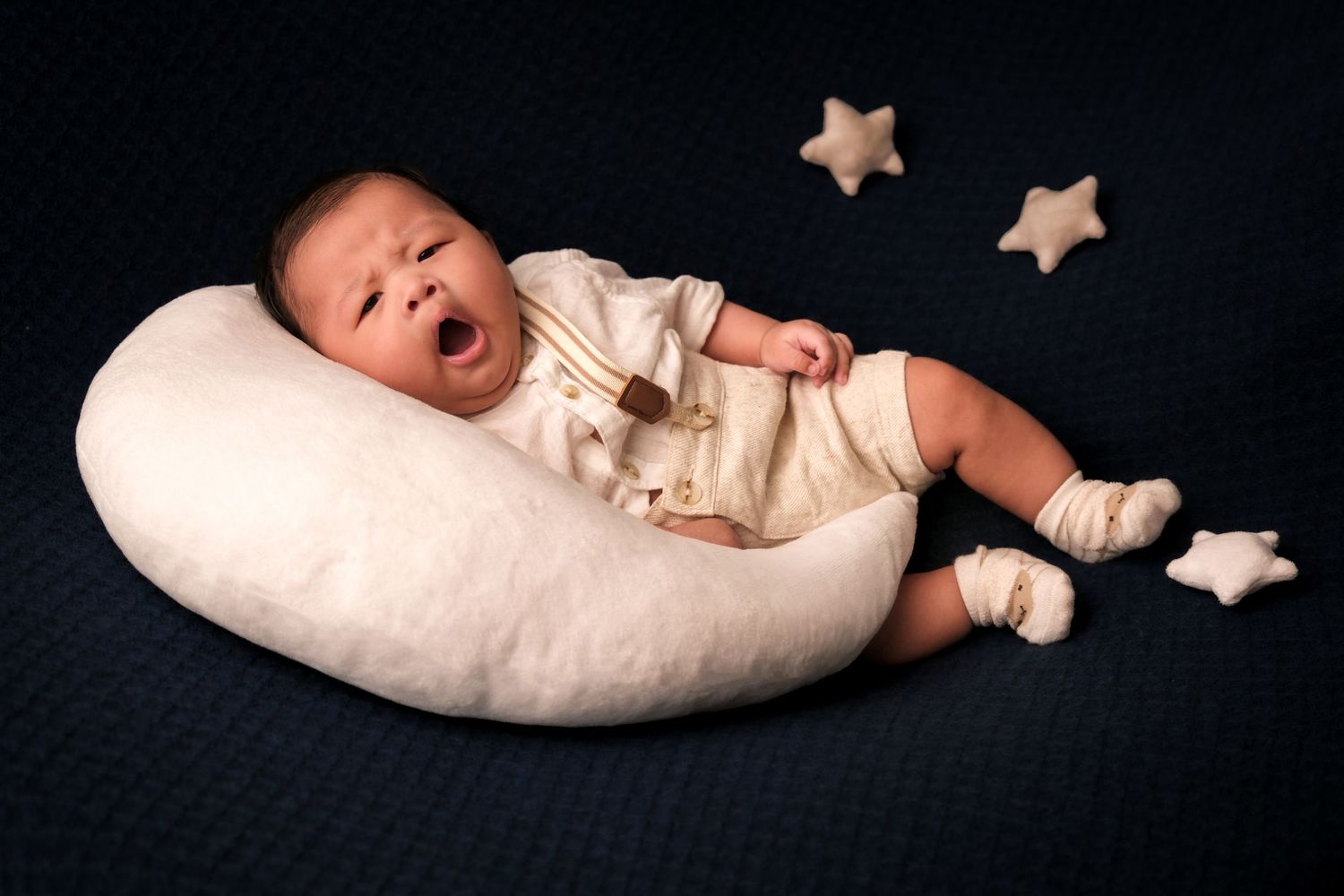 Sleeping newborn on crescent moon pillow with decorative stars in dark setting.