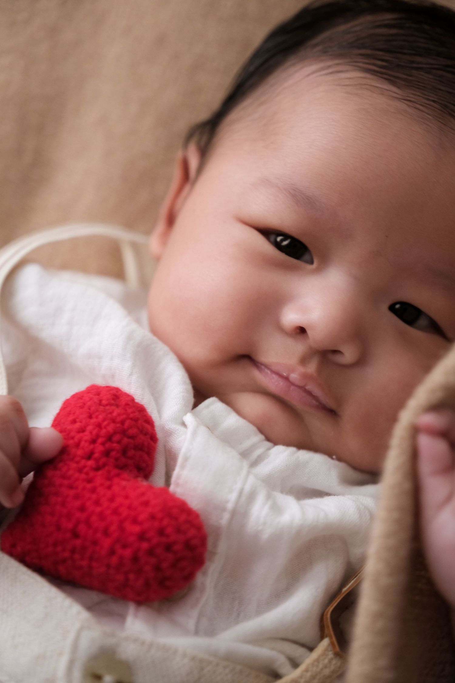 Sweet portrait sequence with red heart prop and white blanket background.