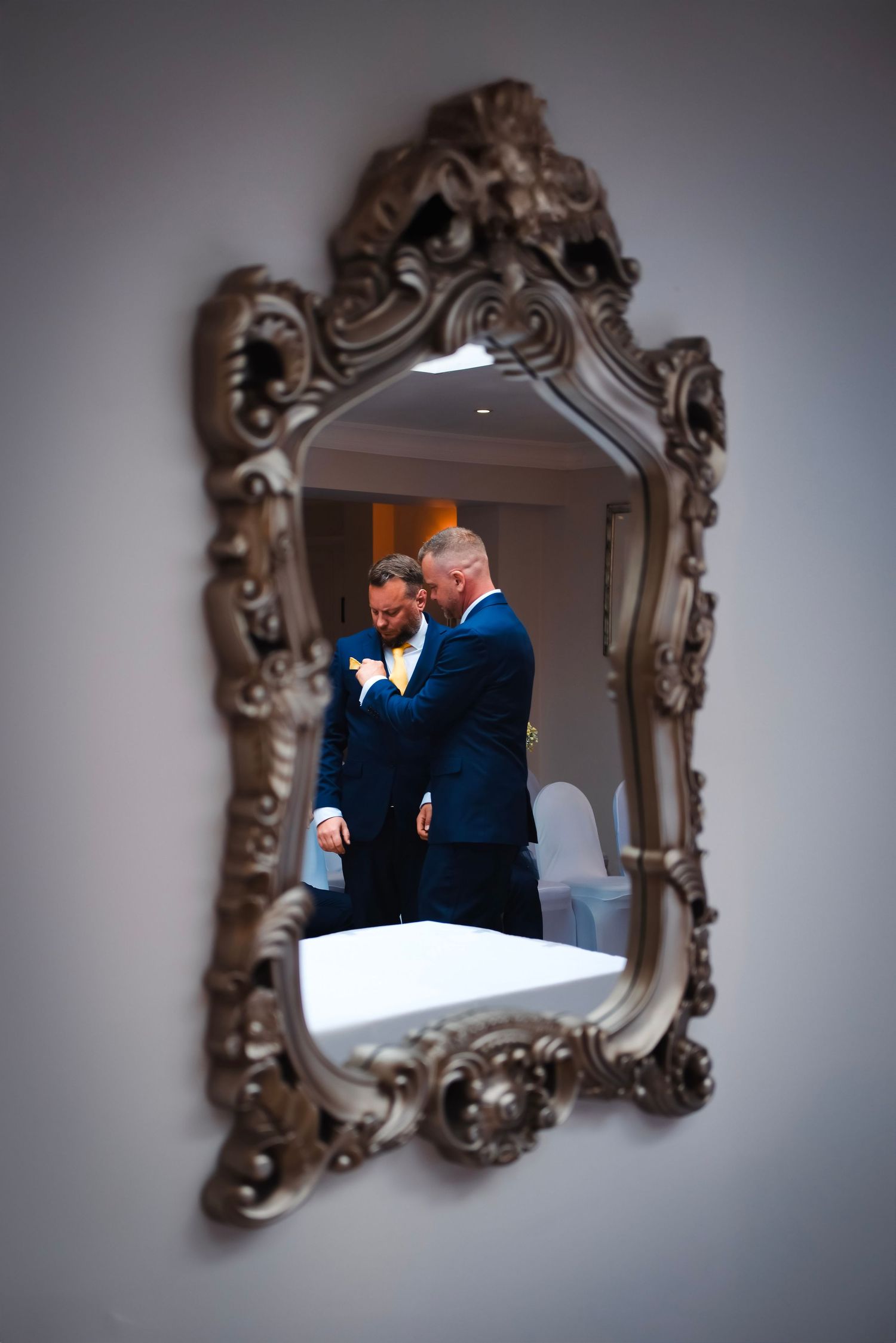 Ornate vintage mirror reflects tender moments against neutral grey wall.