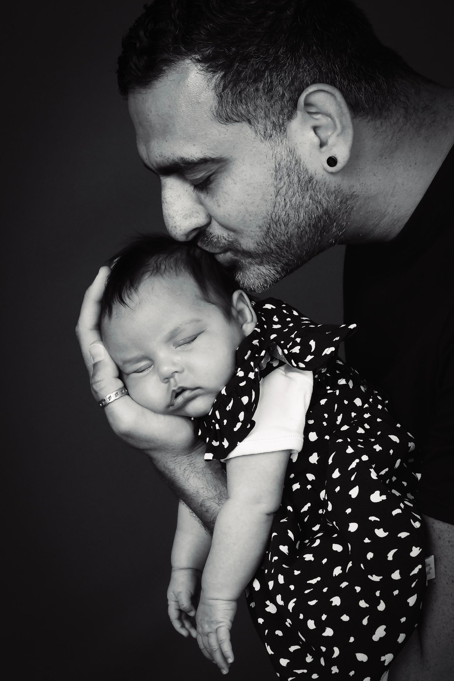 Black and white intimate portrait showing tender family moment against dark background.