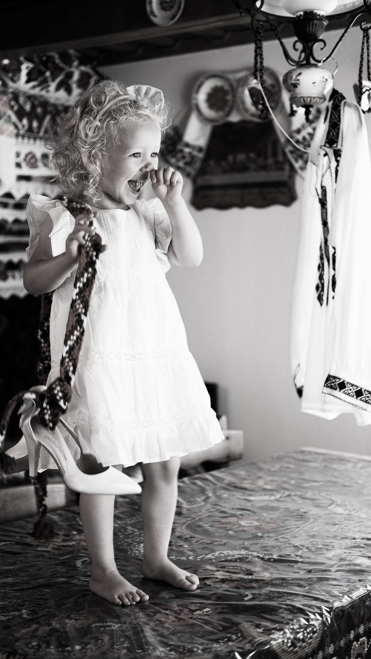 Black and white series of toddler in white dress playing on textured surface.